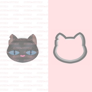 May include: A grey cat face cookie cutter with a pink nose and blue eyes. The cutter is on a white background with a pink background behind it.