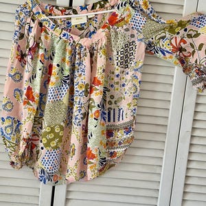 Puede incluir: Una blusa de manga larga con base rosa claro y un patr&oacute;n de patchwork multicolor con dise&ntilde;os florales, de cachemira y geom&eacute;tricos. La prenda tiene un escote en V, tela fruncida en los hombros y pu&ntilde;os el&aacute;sticos en las mangas.