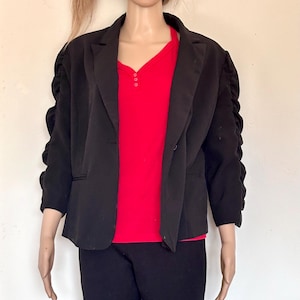 以下が含まれることがあります： ボタンが1つ付いた長袖の黒いブレザー。ブレザーは袖が少し膨らんだデザインです。