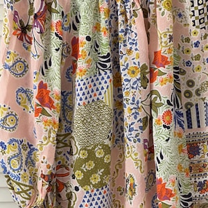 Puede incluir: Una blusa de color rosa claro con un patr&oacute;n de patchwork multicolor que presenta diversos motivos florales, de cachemira y geom&eacute;tricos en tonos naranja, amarillo, verde, azul y blanco. La prenda tiene tela fruncida en el cuello y mangas largas.