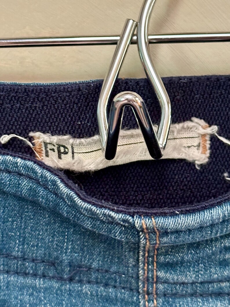 Puede incluir: Primer plano de unos pantalones cortos vaqueros azules con una cintura azul marino. Los pantalones cortos est&aacute;n colgados de una percha de metal plateado. La etiqueta dice "FP".