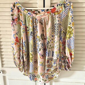 Puede incluir: Una blusa de manga larga con un color base rosa claro y un patr&oacute;n de patchwork multicolor. El dise&ntilde;o incluye varios motivos florales, geom&eacute;tricos y abstractos en tonos azul, verde, amarillo, naranja y rojo. Tiene un escote ancho.