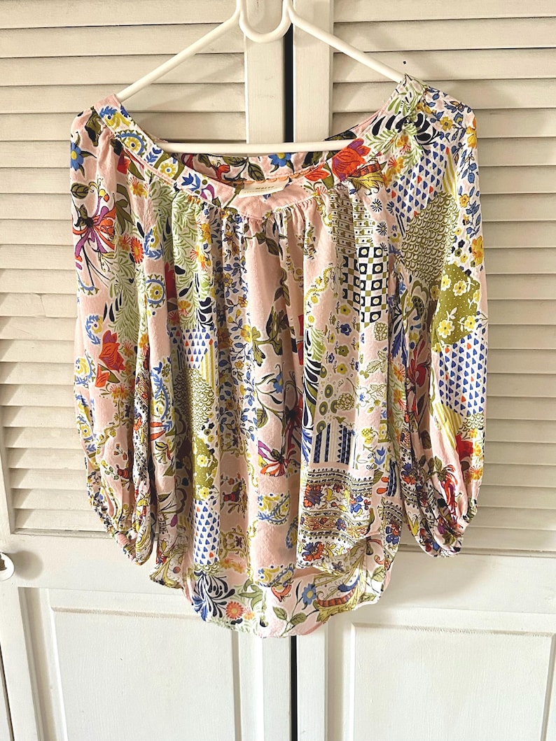 Puede incluir: Una blusa de manga larga con un color base rosa claro y un patr&oacute;n de patchwork multicolor. El dise&ntilde;o incluye varios motivos florales, geom&eacute;tricos y abstractos en tonos azul, verde, amarillo, naranja y rojo. Tiene un escote ancho.