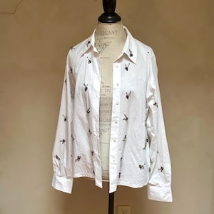 May include: White button-down shirt with long sleeves, adorned with small, dark-colored embroidered details. The shirt is displayed on a mannequin. The text "ABRICANT" and "rs designs" is visible on the mannequin.