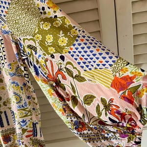 Puede incluir: Una blusa de manga larga con un dise&ntilde;o de patchwork sobre una base de color rosa claro. La tela muestra una variedad de patrones coloridos, incluyendo motivos florales, formas geom&eacute;tricas y estampados bot&aacute;nicos abstractos en azul, verde, naranja y amarillo.
