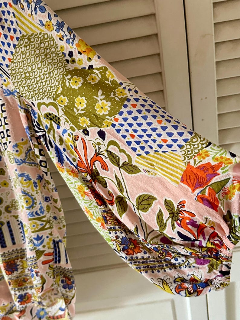 Puede incluir: Una blusa de manga larga con un dise&ntilde;o de patchwork sobre una base de color rosa claro. La tela muestra una variedad de patrones coloridos, incluyendo motivos florales, formas geom&eacute;tricas y estampados bot&aacute;nicos abstractos en azul, verde, naranja y amarillo.
