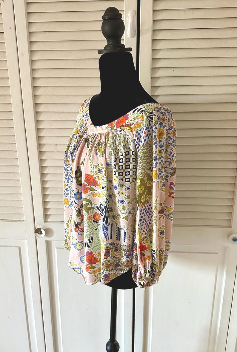 Puede incluir: Una blusa de manga larga con una base de color rosa claro y un patr&oacute;n de patchwork multicolor. El dise&ntilde;o incluye varios motivos florales, formas geom&eacute;tricas y estampados abstractos en tonos azul, amarillo, naranja y verde. Tiene cuello en V.