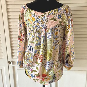 Puede incluir: Una blusa de manga larga con base rosa claro y un patr&oacute;n de patchwork multicolor con dise&ntilde;os florales, bot&aacute;nicos y geom&eacute;tricos. La prenda tiene un escote ancho y redondeado, adem&aacute;s de pu&ntilde;os fruncidos en las mangas.
