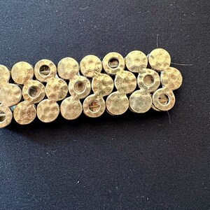 Puede incluir: Un brazalete dorado compuesto por círculos de metal martillado interconectados. El brazalete tiene una superficie texturizada y un cierre de broche. El diseño es simple y elegante, adecuado para el uso diario u ocasiones especiales.