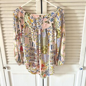 Puede incluir: Una blusa de manga larga con base rosa claro y un patr&oacute;n de patchwork multicolor. El dise&ntilde;o incluye varios motivos florales, de cachemira y geom&eacute;tricos en tonos azul, amarillo, verde y rojo. Tiene un escote ancho y redondeado.
