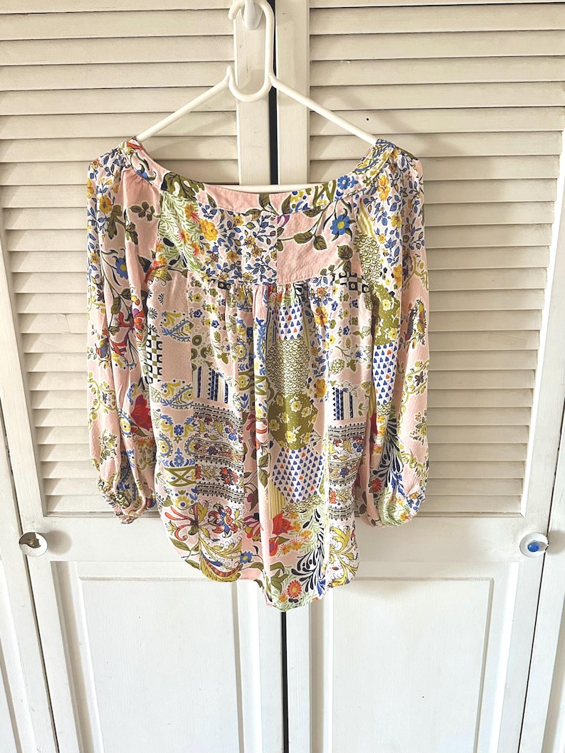 Puede incluir: Una blusa de manga larga con base rosa claro y un patr&oacute;n de patchwork multicolor. El dise&ntilde;o incluye varios motivos florales, de cachemira y geom&eacute;tricos en tonos azul, amarillo, verde y rojo. Tiene un escote ancho y redondeado.