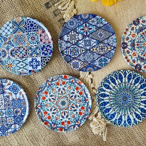 Può includere: Sei sottobicchieri rotondi in ceramica con intricati motivi geometrici in blu, bianco e rosso. I sottobicchieri sono disposti in cerchio su uno sfondo di juta.