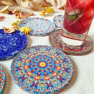 May include: Set of six colorful round coasters with intricate mandala designs. The coasters feature a variety of colors, including blue, red, yellow, and white. The coasters are made of a durable material and are perfect for protecting your furniture from spills and scratches.