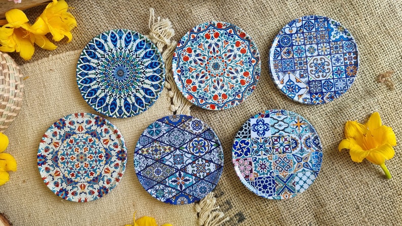 May include: Six round coasters with intricate blue, white, and red geometric patterns. The coasters are made of ceramic and have a glossy finish.