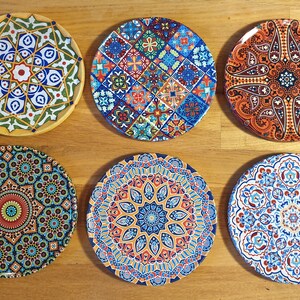 May include: Six decorative ceramic plates with intricate geometric patterns in shades of blue, red, orange, yellow, and green. The plates feature a variety of designs, including floral motifs, paisley patterns, and tile-like designs.
