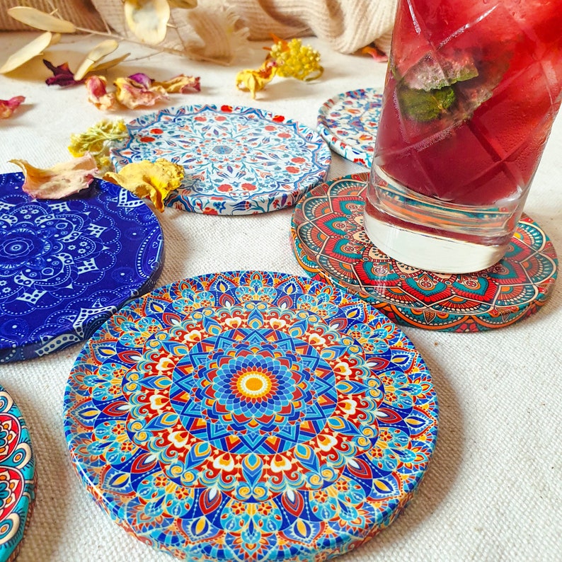 May include: Set of six colorful round coasters with intricate mandala designs. The coasters feature a variety of colors, including blue, red, yellow, and white. The coasters are made of a durable material and are perfect for protecting your furniture from spills and scratches.