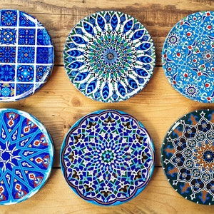 May include: Six decorative ceramic plates with intricate blue, green, and white geometric patterns. The plates feature a variety of designs, including floral motifs, starbursts, and geometric shapes.