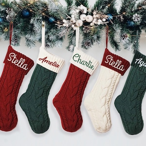 Può includere: Cinque calze di Natale personalizzate con nomi ricamati. Le calze sono realizzate in tessuto a maglia rosso, verde e bianco.