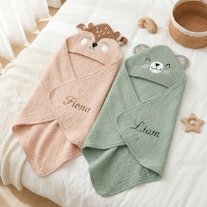 Puede incluir: Dos toallas con capucha para bebé, una rosa con diseño de ciervo y el nombre "Fiona" bordado, y otra verde con diseño de oso y el nombre "Liam" bordado. Las toallas están hechas de tela suave y texturizada.