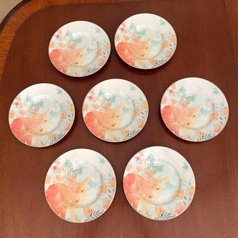 Puede incluir: Conjunto de siete platos decorativos con un dise&ntilde;o caprichoso. Cada plato presenta una imagen central de una vaca de las Tierras Altas en tonos naranja y amarillo, rodeada de acentos florales y de hojas en tonos azules y coral. Los platos tienen un borde dorado. Di&aacute;metro aproximado de 20 cm.