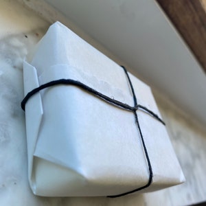 May include: A white package wrapped in paper and tied with black string.