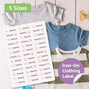 May include: A sheet of personalized iron-on clothing labels with the name "Vivian M." and unicorn, rainbow, and cupcake graphics. The labels are displayed with several children's t-shirts. Text on the image reads "5 Sizes" and "Iron-On Clothing Label."