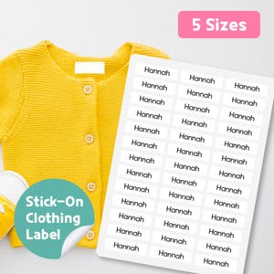 Könnte beinhalten: Eine gelbe Strickjacke mit Knöpfen und ein Paar gelbe Schuhe liegen neben einem Bogen weißer Etiketten mit dem Namen "Hannah". Die Etiketten sind für Kleidung und sind in 5 Größen erhältlich.