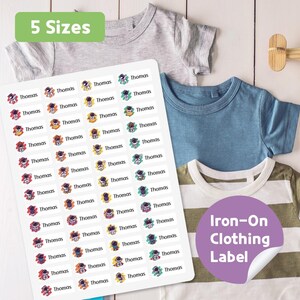 May include: A sheet of iron-on clothing labels with the name "Thomas" and astronaut graphics. The labels are displayed with several children's t-shirts in gray, blue, and white with green stripes. The image also includes text that says "5 Sizes" and "Iron-On Clothing Label."