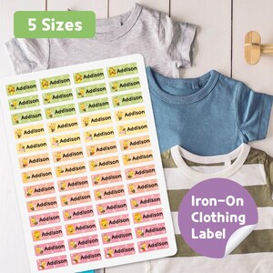 May include: A sheet of iron-on clothing labels with the name "Addison" and a bee graphic. The labels are in various pastel colors. The image also shows several children's t-shirts and text that says "5 Sizes" and "Iron-On Clothing Label."