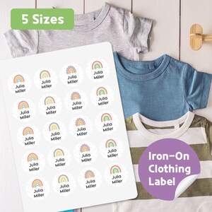 May include: A sheet of round, iron-on clothing labels with rainbow designs and the name "Julia Miller." The labels are displayed with several children's t-shirts in various colors. Text on the image reads "5 Sizes" and "Iron-On Clothing Label."