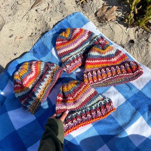 May include: Four colorful striped knit hats on a blue and white checkered blanket. The hats are made with a variety of colors, including red, orange, yellow, green, blue, and purple.