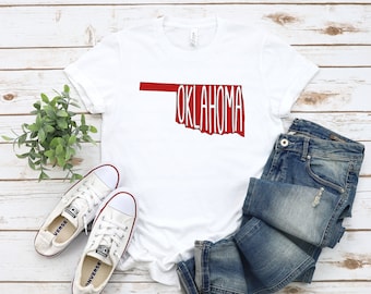 May include: White t-shirt with a red outline of the state of Oklahoma and the word "OKLAHOMA" written in white inside the outline.