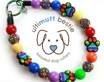 Puede incluir: Un collar de perro de cuentas de colores con dijes de pata de perro arcoíris. El collar está hecho con una variedad de cuentas, incluyendo colores sólidos, cuentas multicolores y cuentas texturizadas. El collar está unido a un llavero. El texto "ultimutt bestie beaded dog collars" está impreso sobre un fondo blanco.