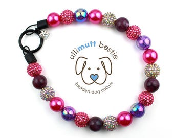 Puede incluir: Un collar de perro con cuentas de colores, con cuentas rosas, moradas e iridiscentes. El collar tiene un cierre negro y el logotipo dice "ultimutt bestie beaded dog collars".