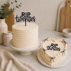 Peut inclure: Deux gâteaux, un rond et un en forme de cœur, avec un glaçage blanc. Le gâteau rond a un cake topper noir "RIP twenties". Le gâteau en forme de cœur a un cake topper noir "RIP thirties" et des décorations de nœuds noirs.