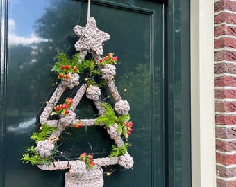 May include: A beige crocheted Christmas tree wreath with a star on top, decorated with greenery and red berries. The wreath is hanging on a dark green door.