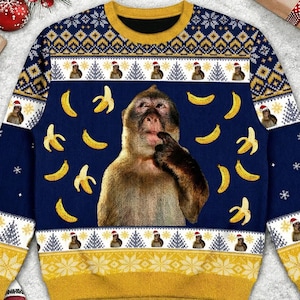 Peut inclure: Pull-over bleu marine avec un singe, des bananes et des bonnets de Père Noël. Le pull a un col, des poignets et un ourlet jaunes. Le motif comprend des flocons de neige et des sapins, créant un thème de vacances festif.