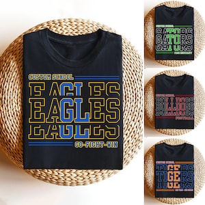 以下が含まれることがあります： 黒いTシャツ。カスタムスクールのデザイン。1枚は青と黄色の「EAGLES」と下の「GO-FIGHT-WIN」が特徴。他のシャツは様々な色の「GATORS」、「BULLDOGS」、「TIGERS」を表示。すべてのシャツの上部に「CUSTOM SCHOOL」と表示。