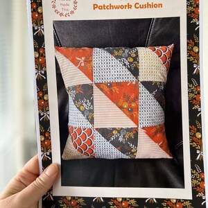 May include: A printed pattern for a scrappy fall patchwork cushion. The pattern features a wreath with the text "Frankie Made This". The pattern includes a photo of a finished cushion with a black, orange, and white patchwork design.