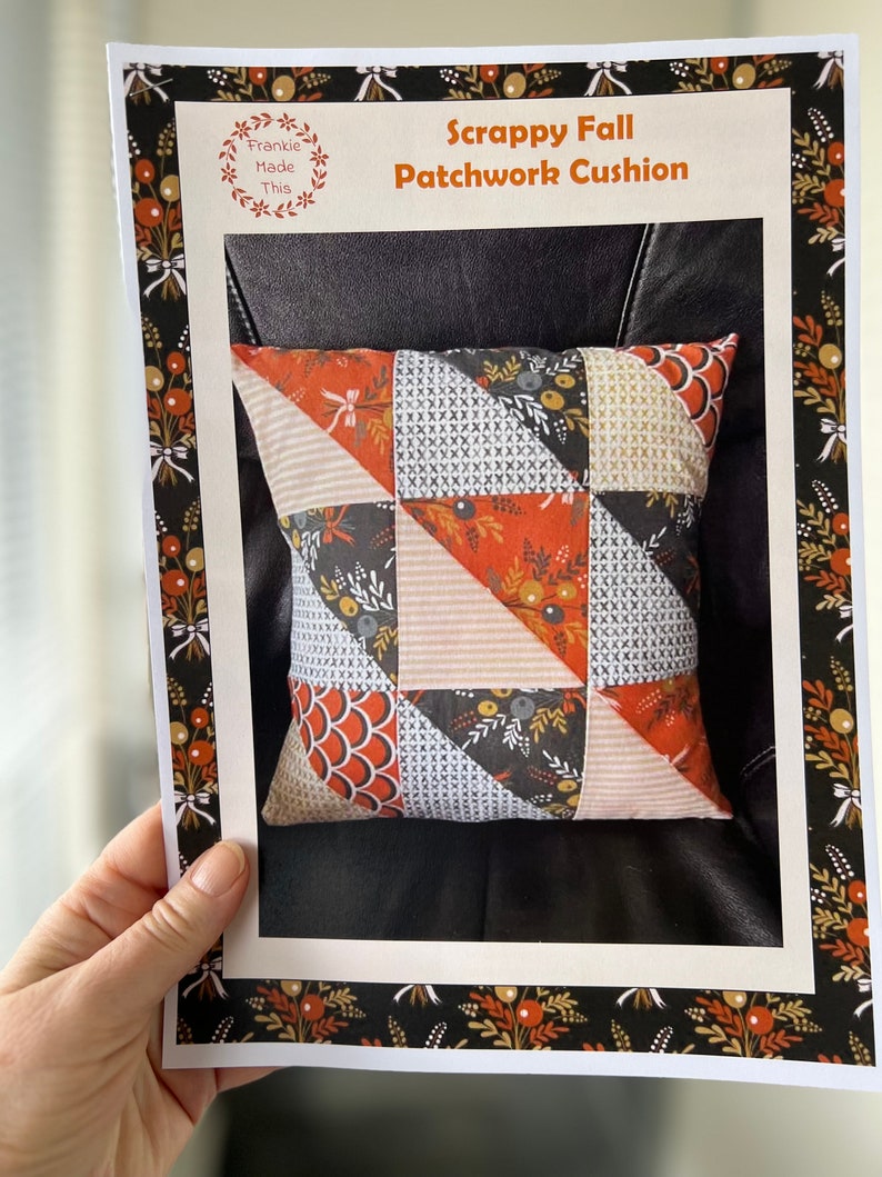 May include: A printed pattern for a scrappy fall patchwork cushion. The pattern features a wreath with the text "Frankie Made This". The pattern includes a photo of a finished cushion with a black, orange, and white patchwork design.