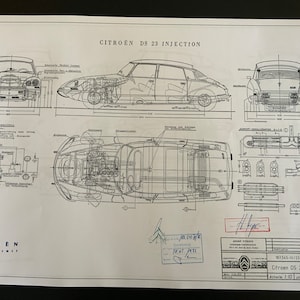 May include: A black and white technical drawing of a Citroen DS 23 Injection car. The drawing shows the car from different angles, including front, side, and top views. The drawing includes measurements in centimetres.