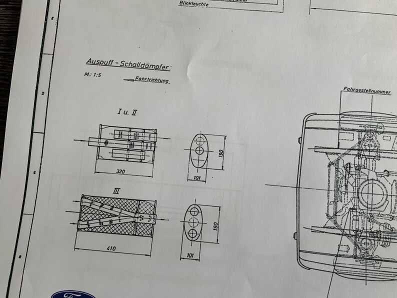Puede incluir: Un dibujo t&eacute;cnico en blanco y negro de un sistema de escape con dimensiones indicadas en cent&iacute;metros. El dibujo muestra el sistema de escape en tres configuraciones diferentes: I y II, III y una vista completa del sistema. El dibujo incluye el texto "Auspuff-Schalld&auml;mpfer" y "Fahrtrichtung".