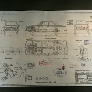 May include: A blueprint-style print of a vintage BMW 2002 car. The print includes multiple views of the car, technical diagrams, and measurements. The text "2002 Typezeichnung" is visible at the bottom. Measurements are in cm.