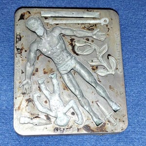 May include: A vintage metal mold featuring a classical male figure, a smaller figure, and various accessories. The mold is rectangular with the text "©1966 BANNER PROD INC" and "©1966 MATTEL INC". The number "4492-051" is also visible.