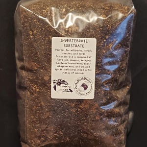 May include: A clear plastic bag filled with invertebrate substrate. The substrate is a mix of dark brown materials, including flake soil, compost, and decaying leaves. A white label with black text reads "INVERTEBRATE SUBSTRATE". The bag is held by a gloved hand.
