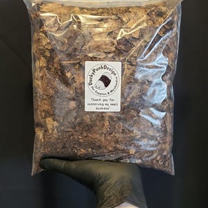 May include: A clear plastic bag filled with brown, dried leaves. The bag is held by a gloved hand. A label on the bag reads "Ducky Punk Design" and "Thank you for supporting my small business!"
