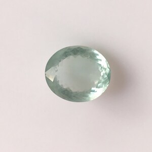 Puede incluir: Una piedra preciosa ovalada de color verde claro con un corte facetado.