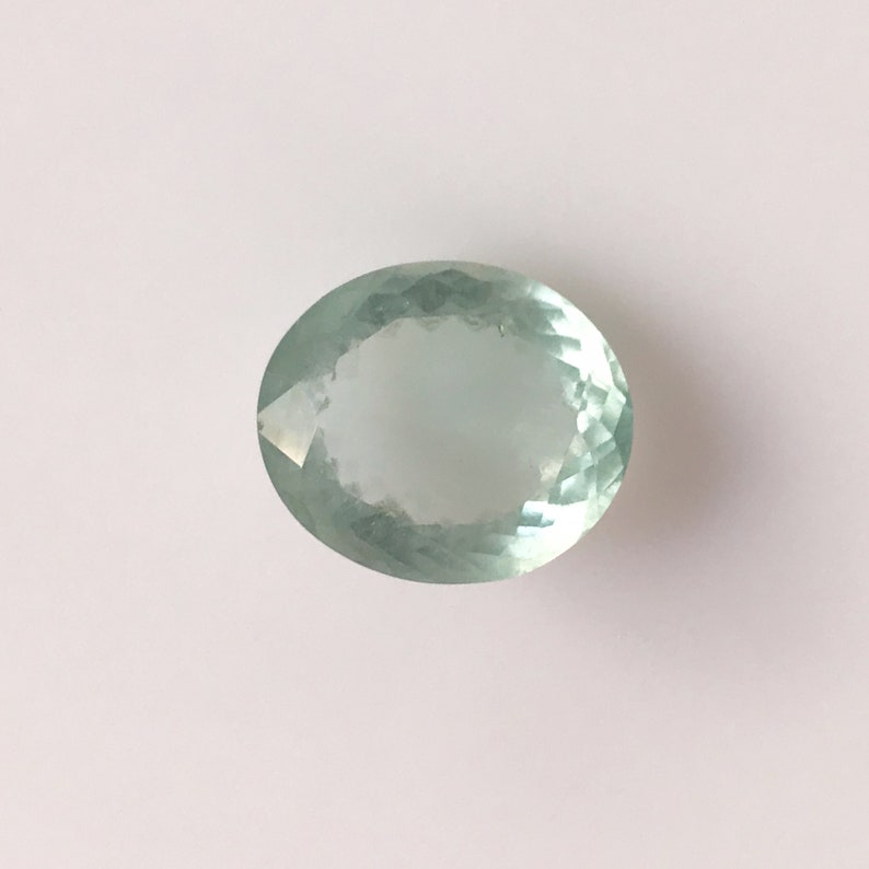 Puede incluir: Una piedra preciosa ovalada de color verde claro con un corte facetado.