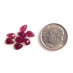 May include: A cluster of ten small, pear-shaped, pink gemstones, arranged in a cluster. The gemstones are approximately the size of a ten pence coin.