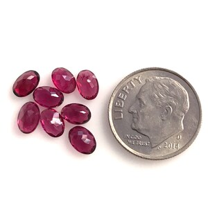 K&ouml;nnte beinhalten: Acht ovale, facettierte, dunkelrosa Edelsteine, etwa so gro&szlig; wie eine Zehn-Cent-M&uuml;nze.